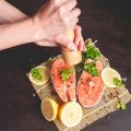 A woman sprinkles salmon with pepper from a pepper mill.