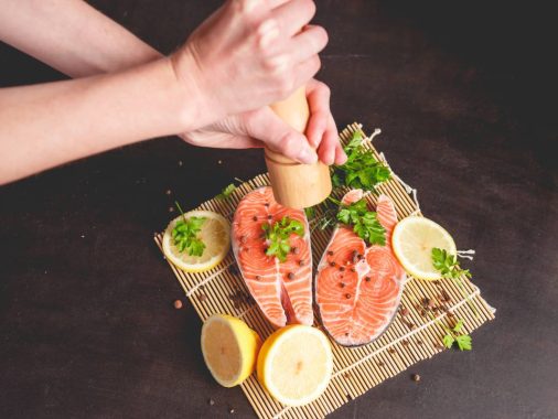 A woman sprinkles salmon with pepper from a pepper mill.